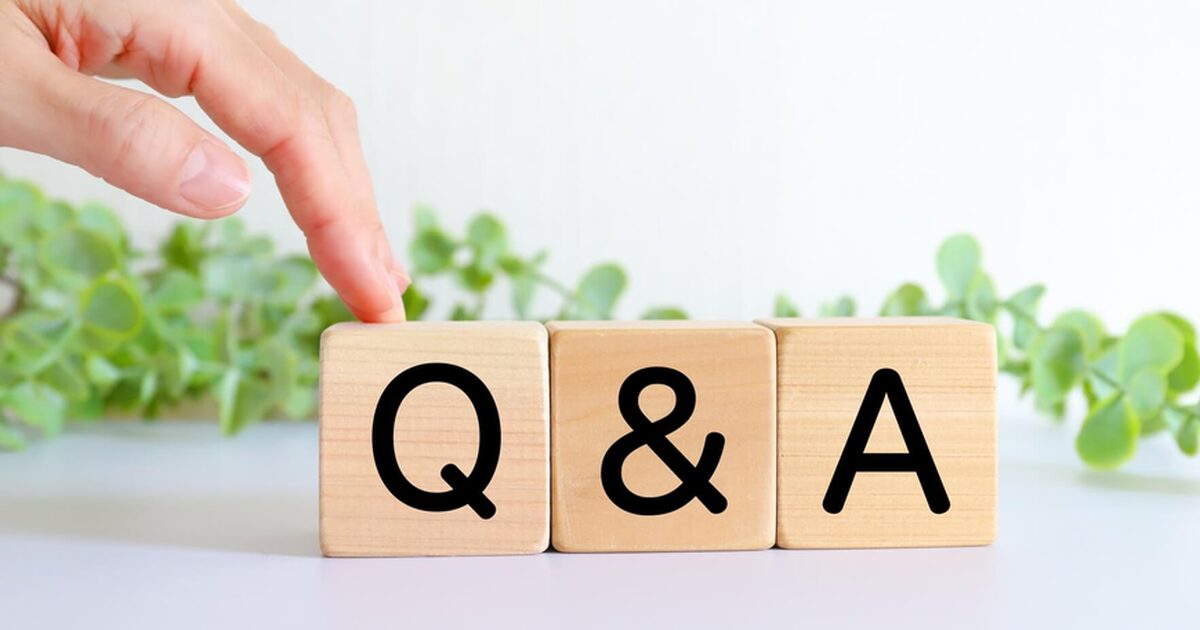 alt="木製ブロックに黒い大文字で「Q」「&」「A」が並び、左上から伸びた指がQブロックをそっと押さえる。背景は白くぼかした観葉植物で、明るく清潔感のある質問コーナーをイメージした写真"